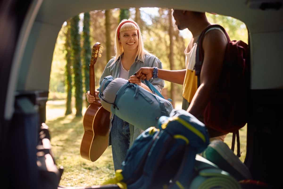Zwei junge Reisende laden ihre Rucksäcke am Auto im Wald, bereit für ihren Campingausflug.