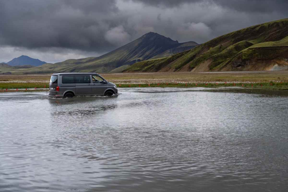A 4WD campervan drives on a waterlogged Icelandic road in what looks like a rocky desert area with little vegetation.