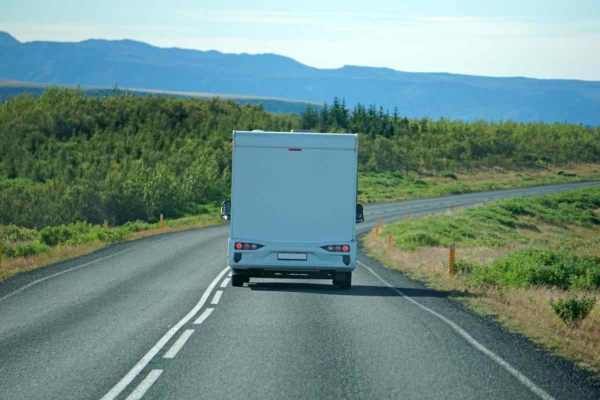 Rear view of a motorhome driving a winding two-lane road through green Icelandic countryside.