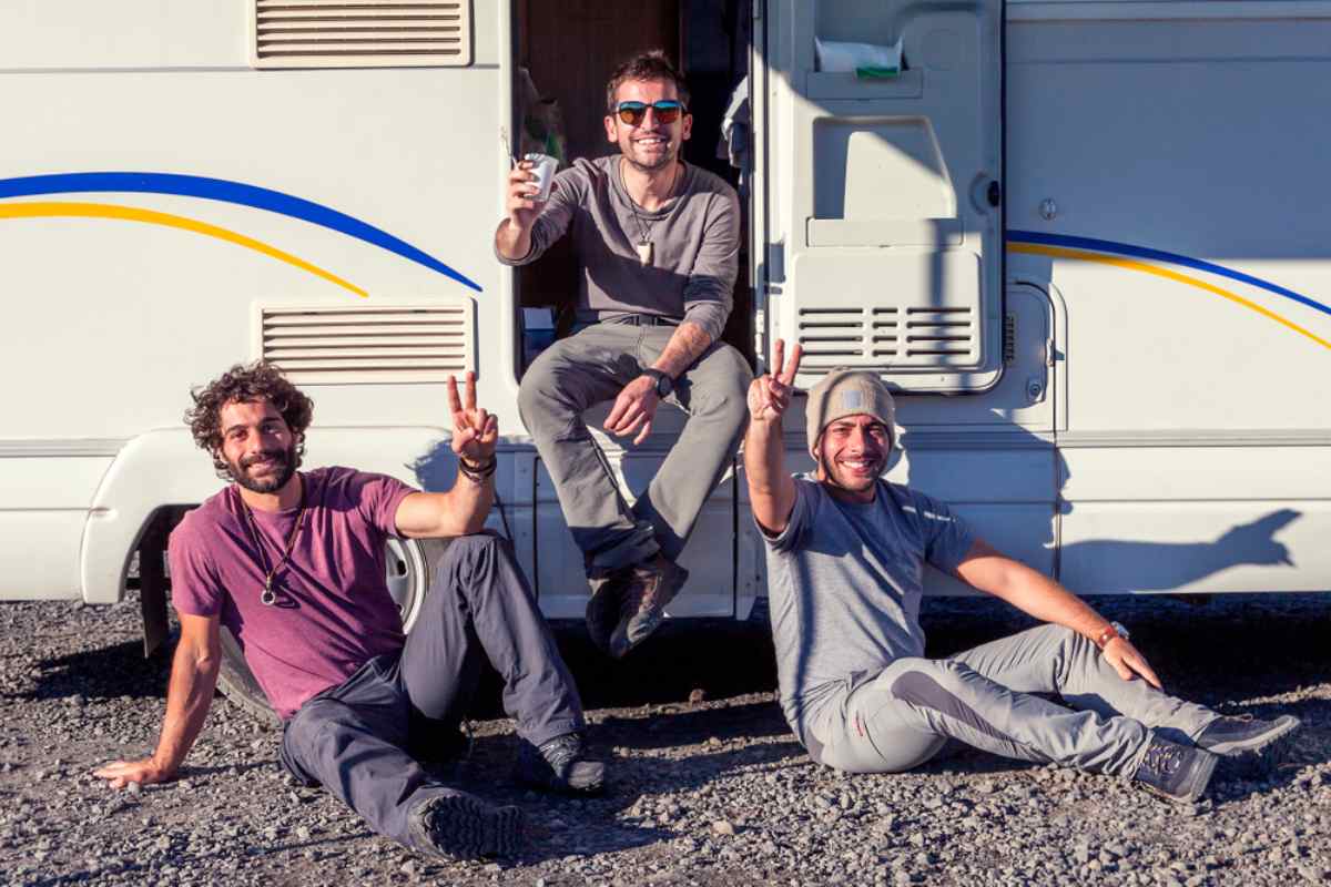 Three friends posing with peace signs beside a white motorhome during an Iceland road trip.