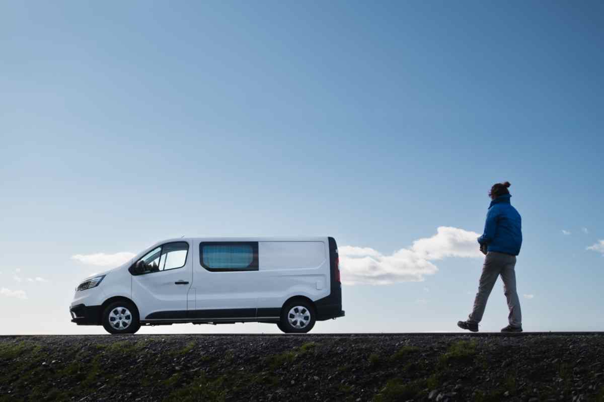 Traveler walking beside a parked white camper van under a clear blue Icelandic sky.