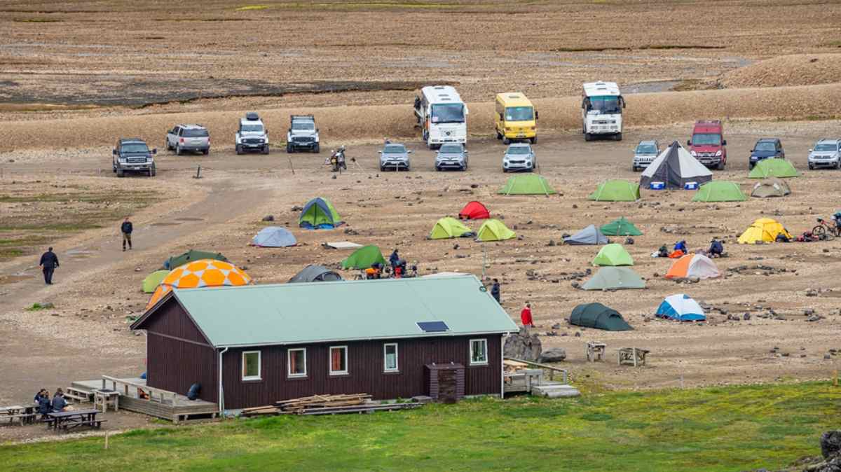 Busy Icelandic campground with colorful tents, 4x4s, and campervans next to a simple service hut.