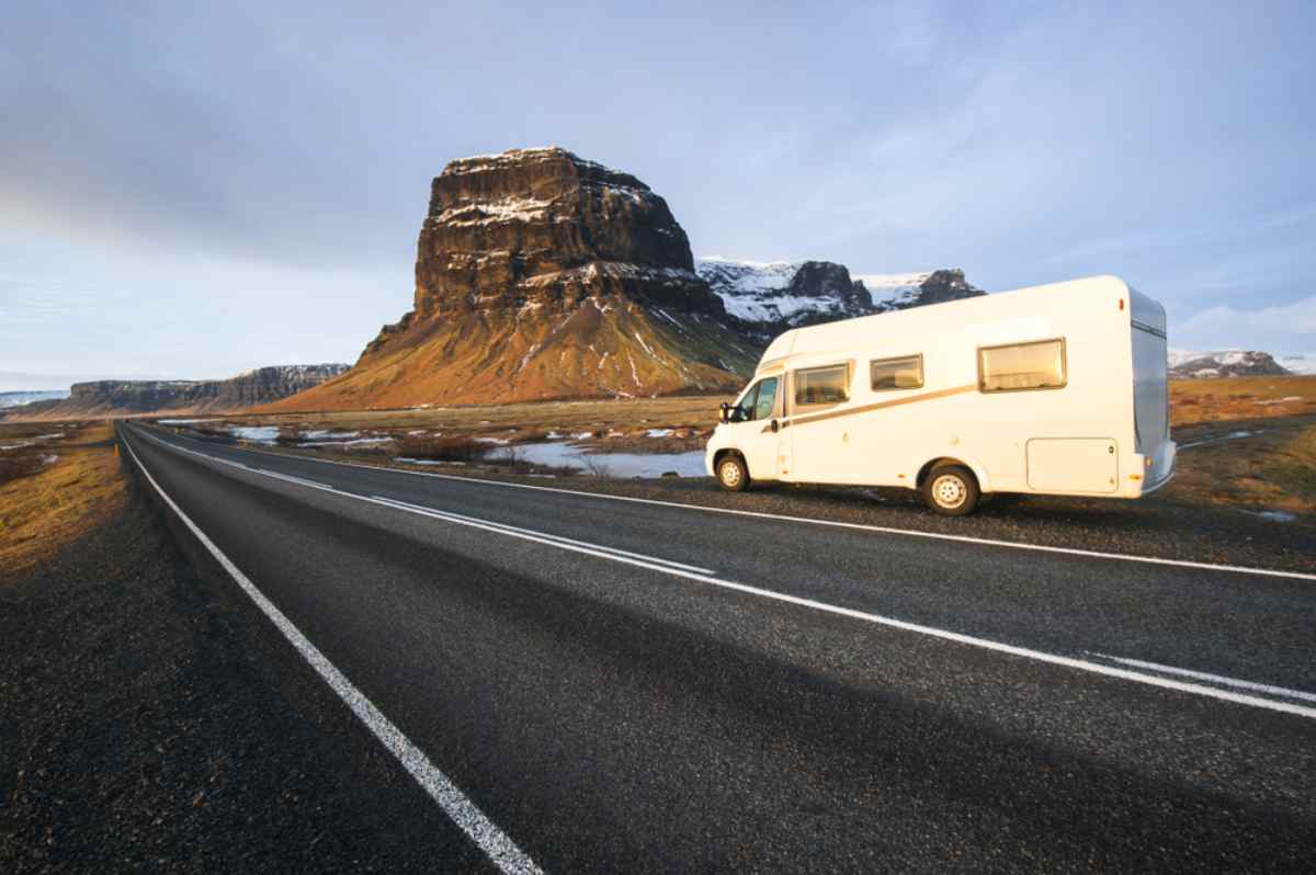 White motorhome parked by an empty highway with a dramatic flat-topped mountain in the background.