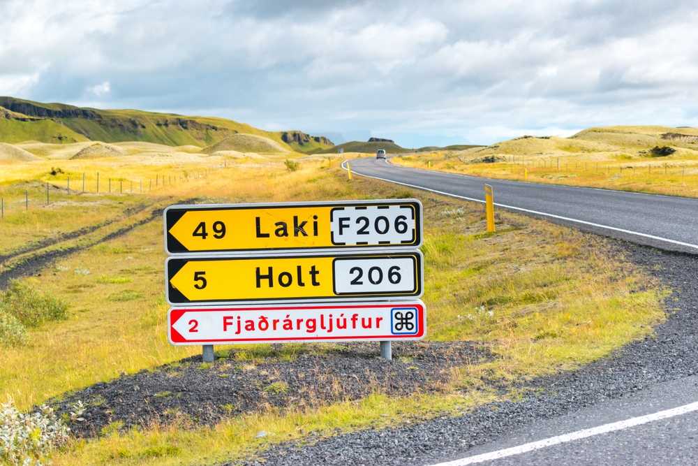 Iceland road sign pointing to Laki on F206 and H&oacute;laskj&oacute;l, with open summer hills in the background.