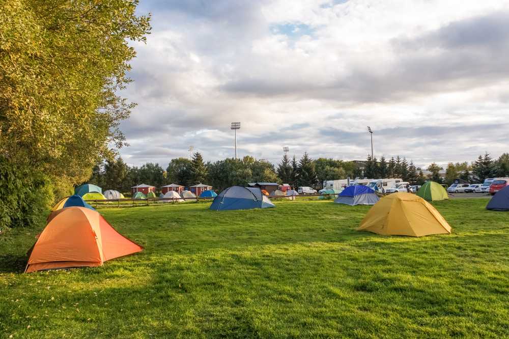 Colorful tents set up on green grass at a Reykjavik campsite with RVs and cabins in the distance.
