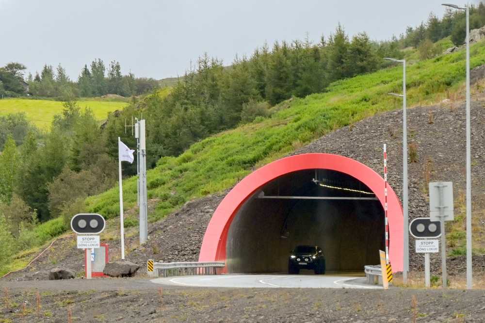 Car entering an Icelandic tunnel with a red arch, stop lights, and green hillsides around the entrance.