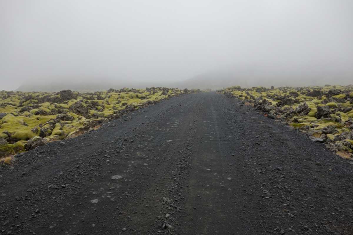 Foggy gravel road in Iceland surrounded by moss-covered lava fields