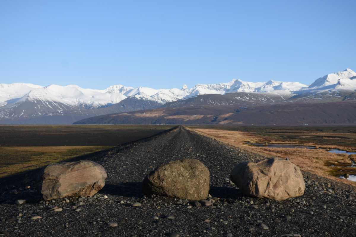 Gravel road in Iceland blocked by large rocks with snow-covered mountains in the background