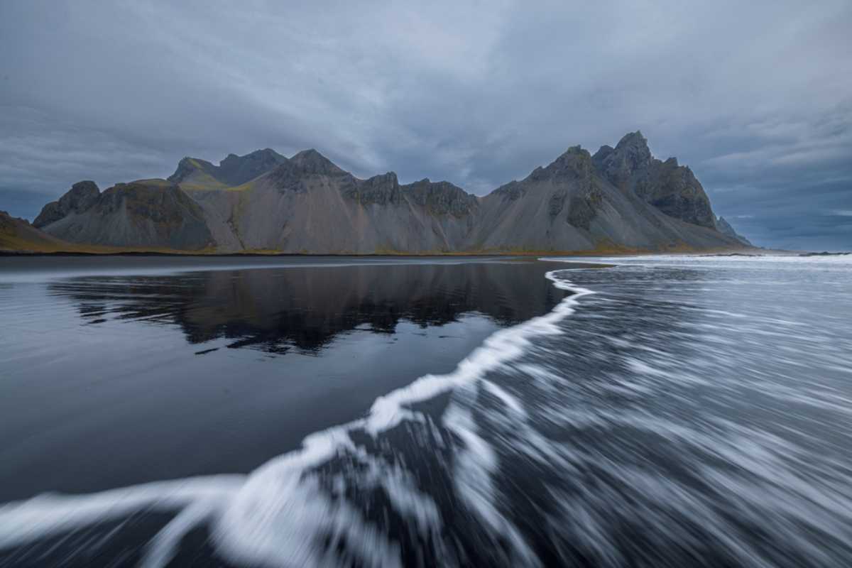Dark storm clouds hanging over Iceland&rsquo;s black sand beach with rugged mountains in the distance