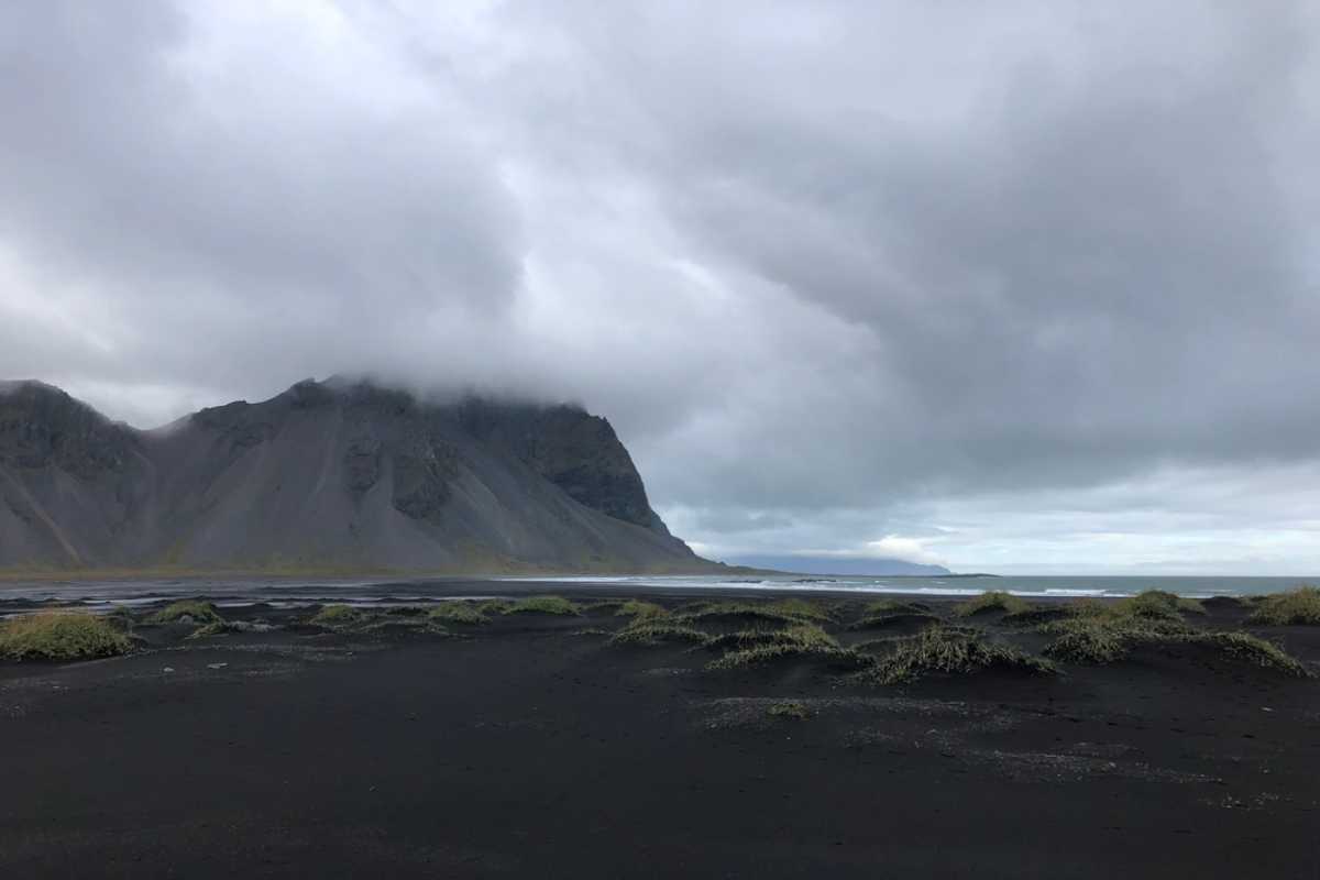 Black sand beach and dramatic coastal mountain in Iceland under low gray clouds