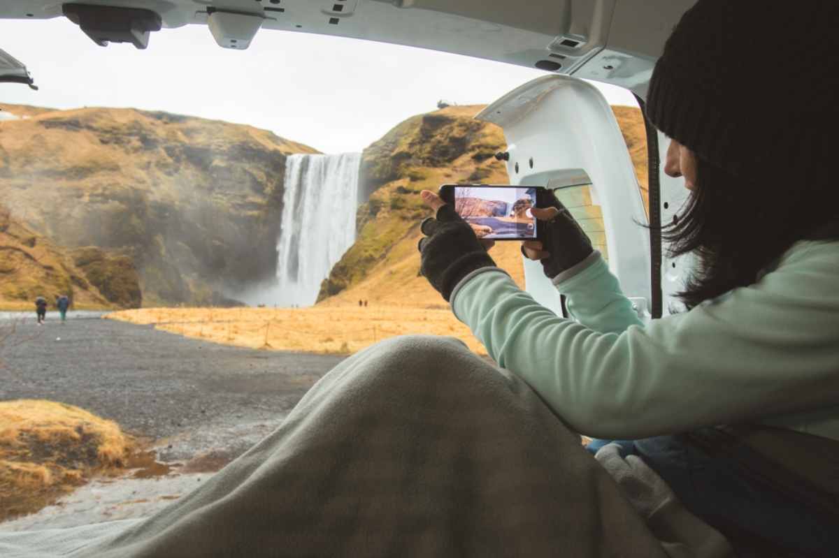 Tourist taking a picture of Skogafoss waterfall from the interior of her cozy campervan