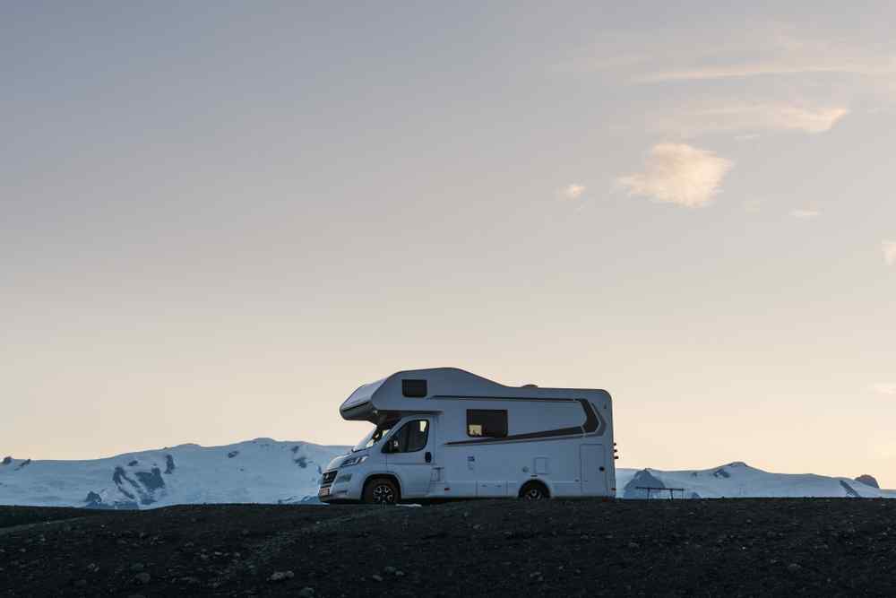 Renting a motorhome in Iceland Motorhome parked beside snowy mountains in Iceland at sunset.