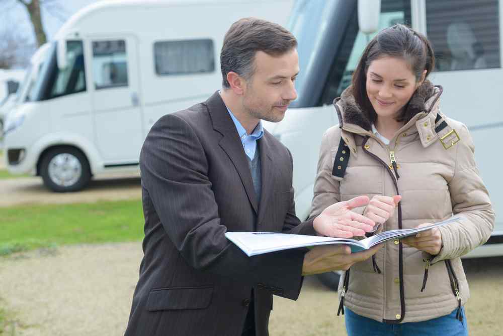 What is already included in your rental Rental agent explaining motorhome rental documents to a woman in front of several parked campervans.