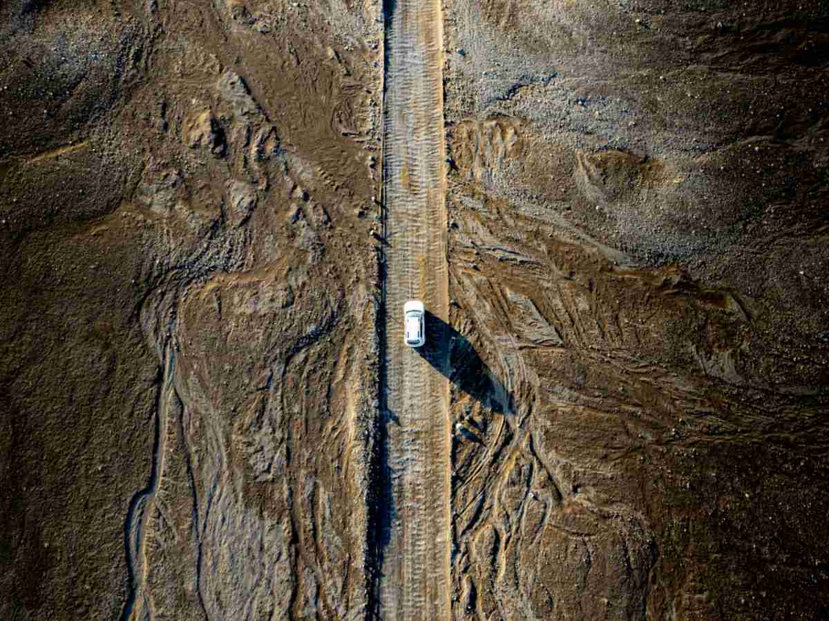 A white vehicle drives on an Icelandic road surrounded by rock materials