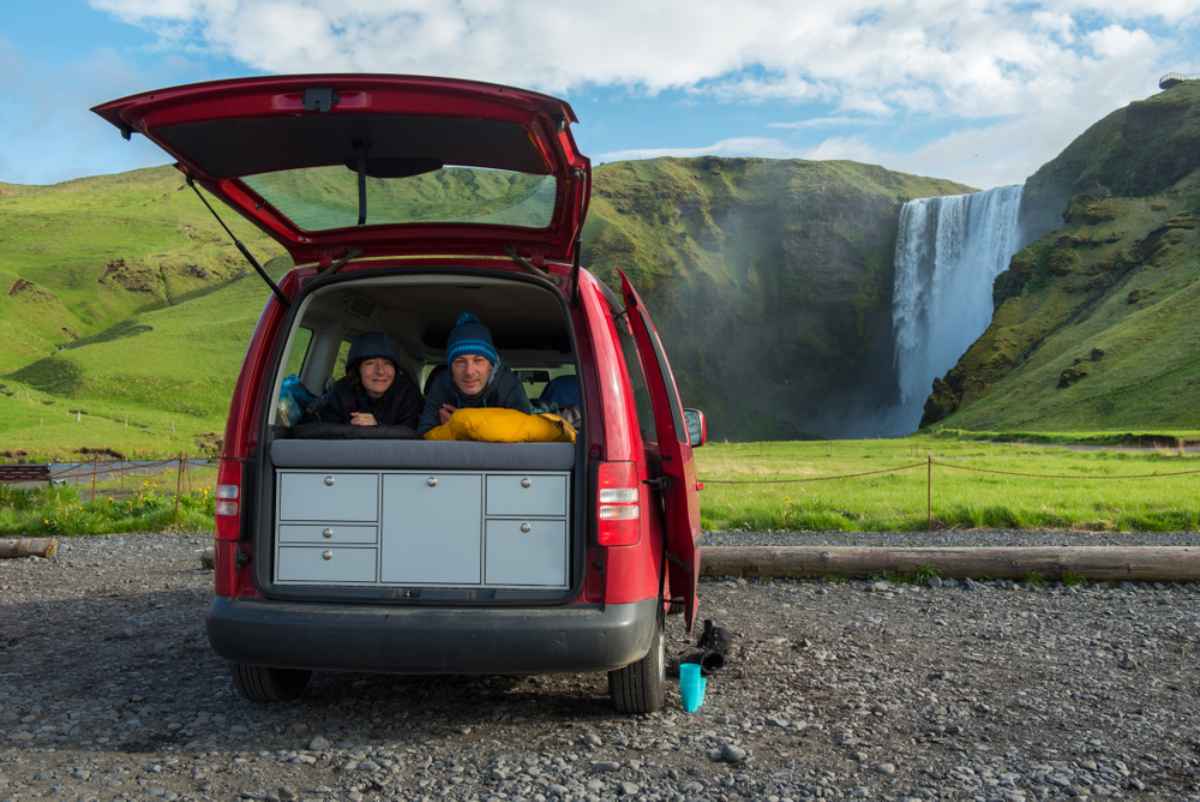 A couple of hikers enjoy the beautiful views of a waterfall in Iceland from inside their camper van.
