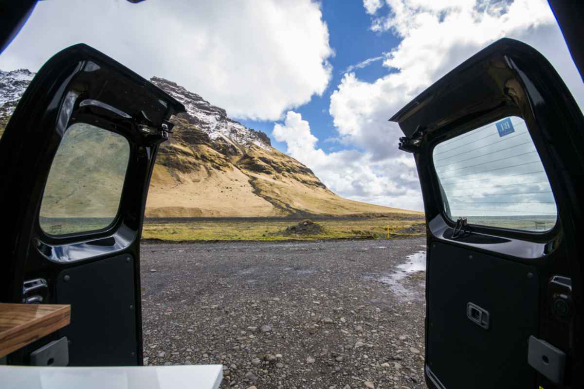 The doors of a camper remain open while overlooking an Icelandic beach.