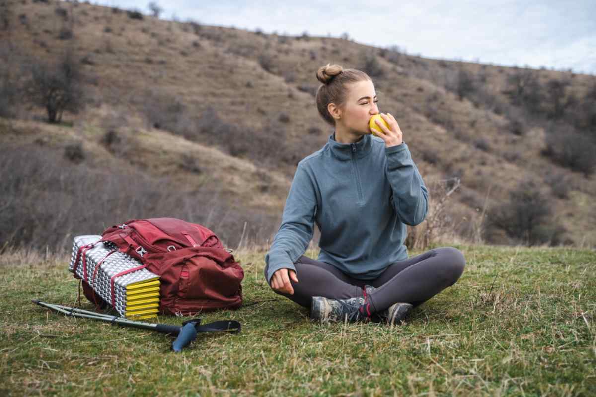 Female hiker sitting on grass eating an apple beside her backpack and trekking pole during a quiet break in a remote Icelandic landscape.