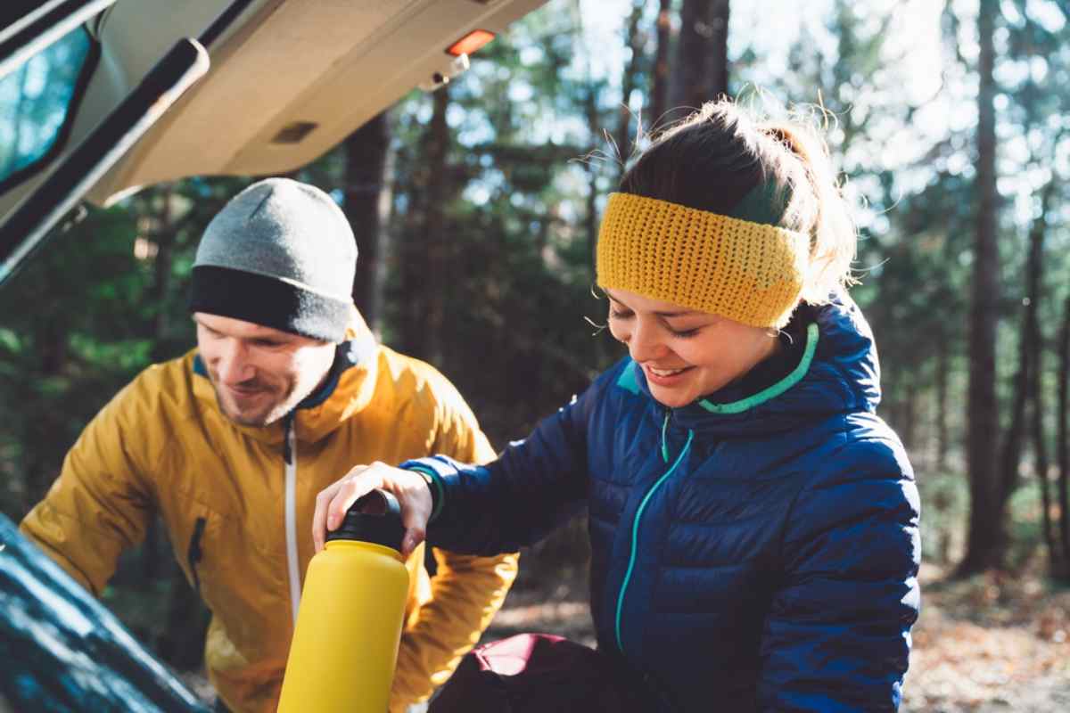 Smiling couple in warm hiking clothing preparing gear at the back of their vehicle before starting a day of outdoor adventure.