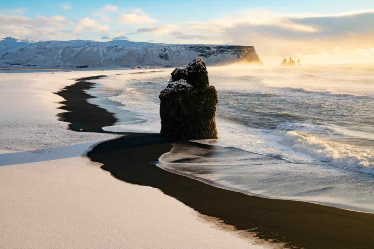 Black sand beach of Reynisfjara in Iceland Snow-dusted black sand beach with crashing waves, sea stacks, and soft sunrise light.