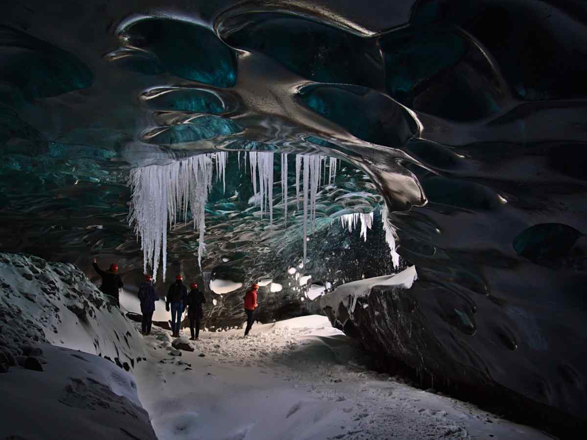 Ice cave in Iceland People exploring a blue ice cave with long icicles hanging from the ceiling.