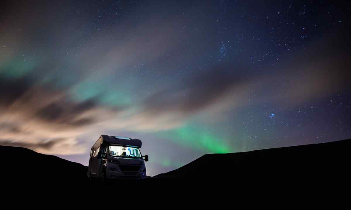 Northern lights during Winter in Iceland RV parked under a starry sky with aurora borealis glowing on the horizon.