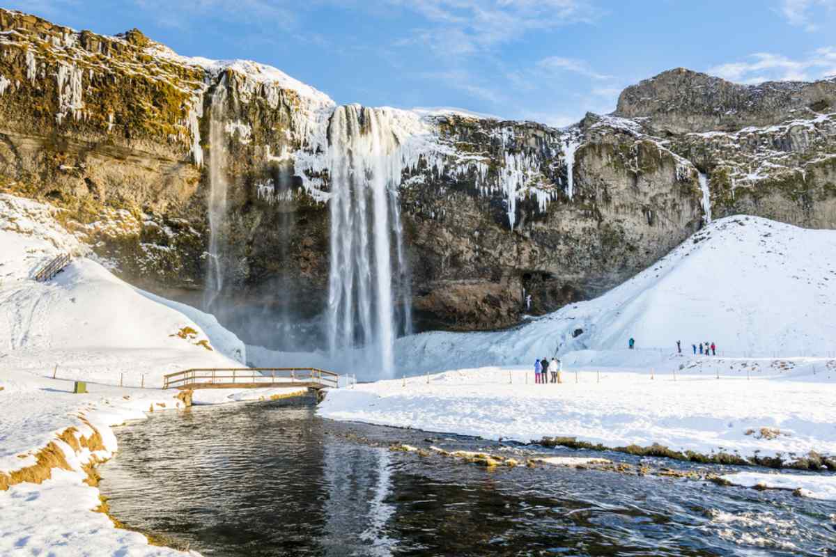 Seljalandsfoss during Winter Seljalandsfoss waterfall framed by snow and ice with visitors on the snowy path below.