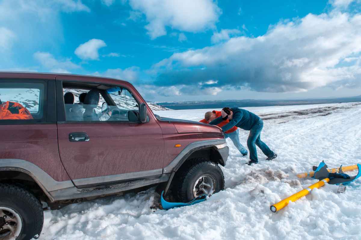A group of men try to push a 4x4 vehicle that is stuck in the snow.