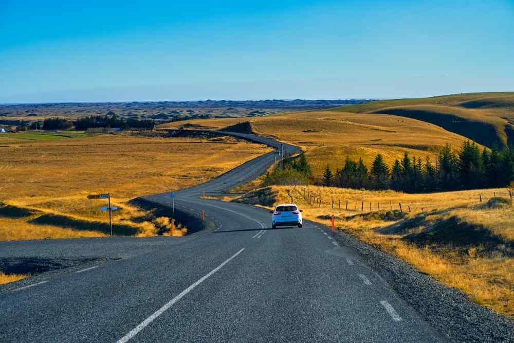 Car driving along a quiet rural road through golden Icelandic countryside in summer.