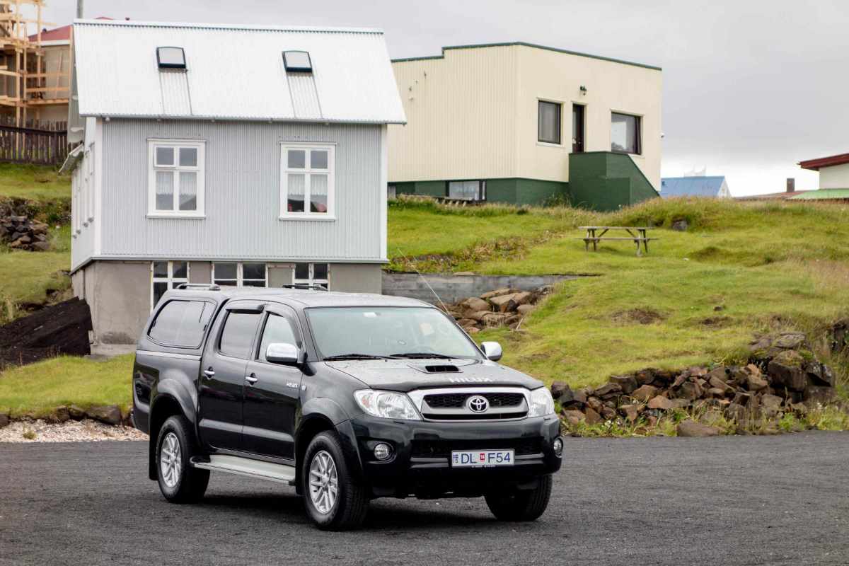 Black Toyota Hilux parked in a small Icelandic village with grassy houses in the background.