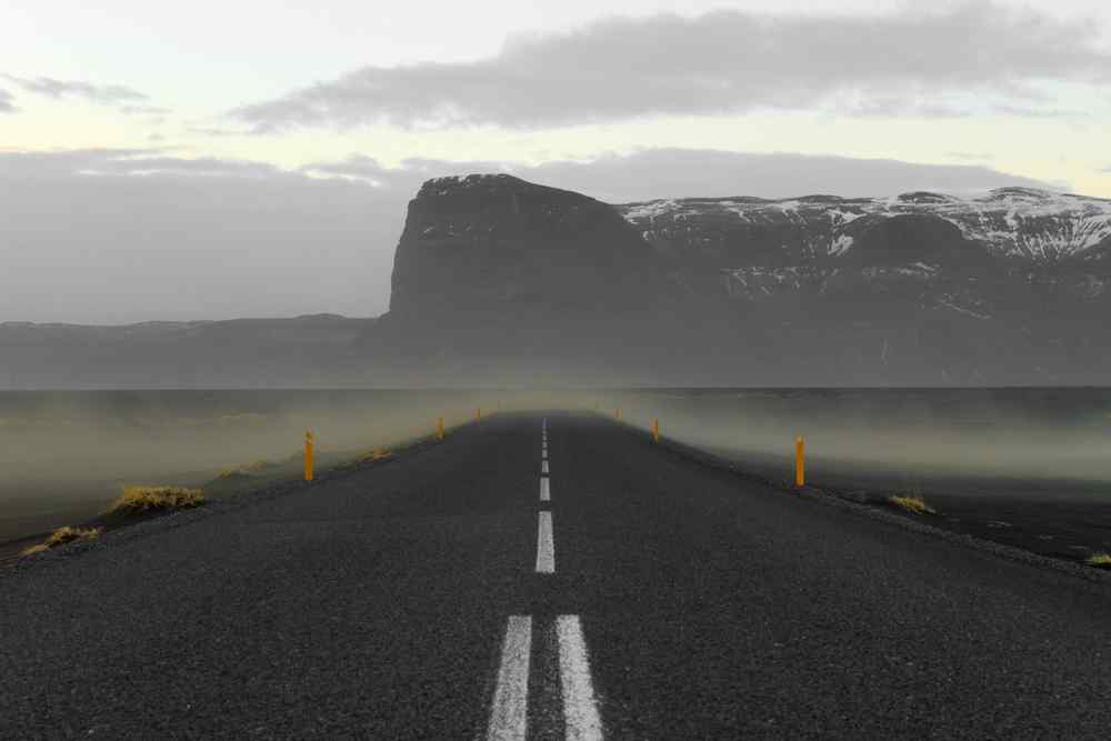 Empty Icelandic road disappearing toward dark mountains in windy, foggy weather.