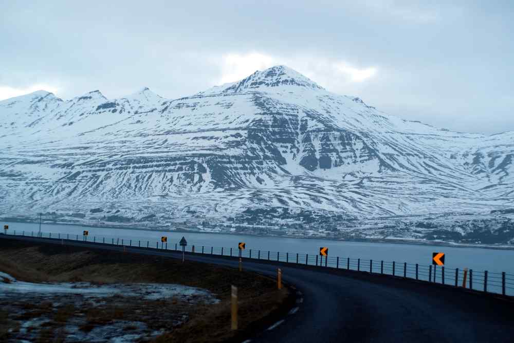 Snow-covered mountain road curving along a fjord in winter in Iceland.