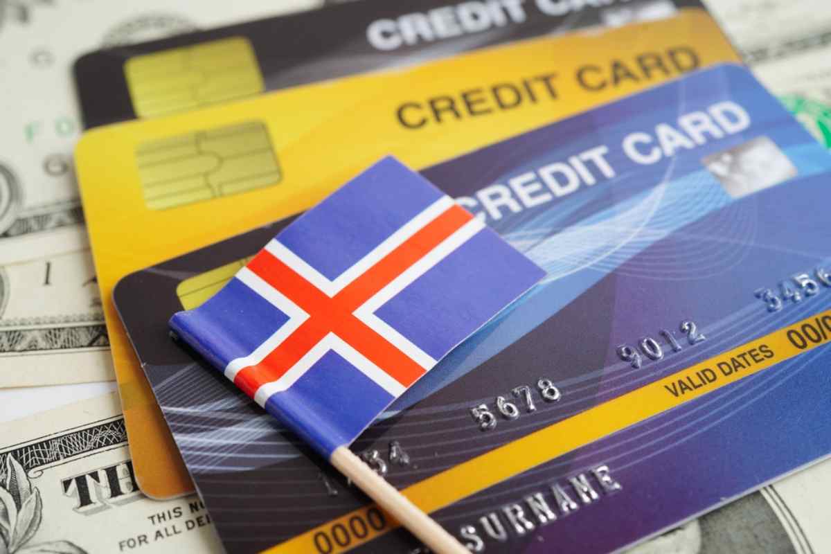 Close-up of Icelandic flag on top of several colorful credit cards and US dollar bills, symbolizing money and payments when traveling in Iceland