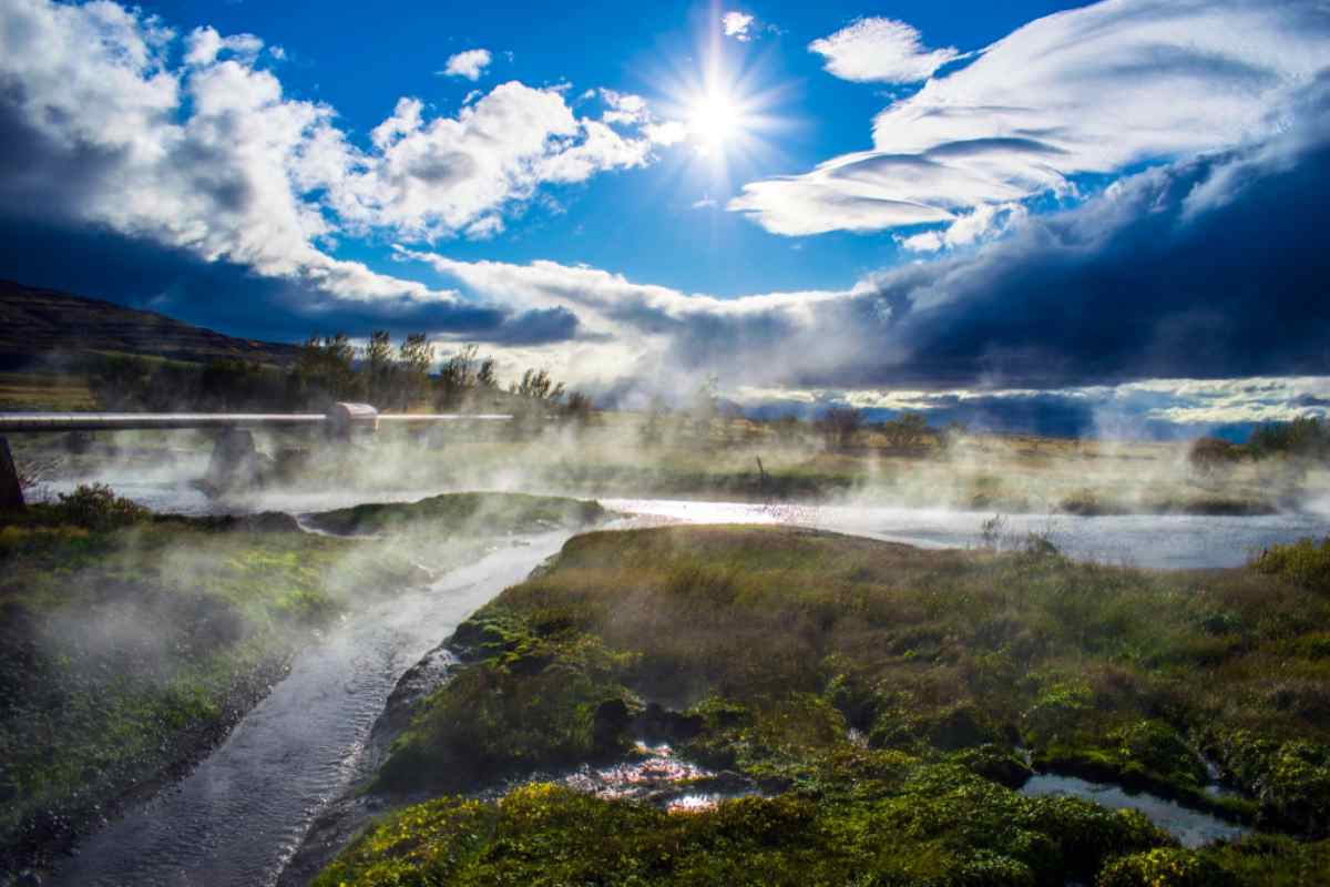 Steam rising from a geothermal river and hot springs under dramatic clouds and bright sun in a wild volcanic landscape in Iceland