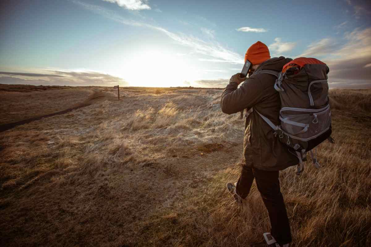 Hiker with large backpack and orange beanie calling for help on a deserted trail at sunset in a windy grassland landscape in Iceland
