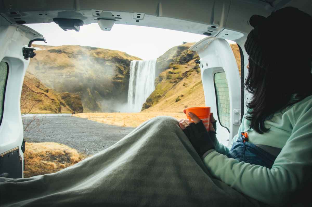 Woman enjoying a cup of coffee from her camper while watching the impressive views of a waterfall