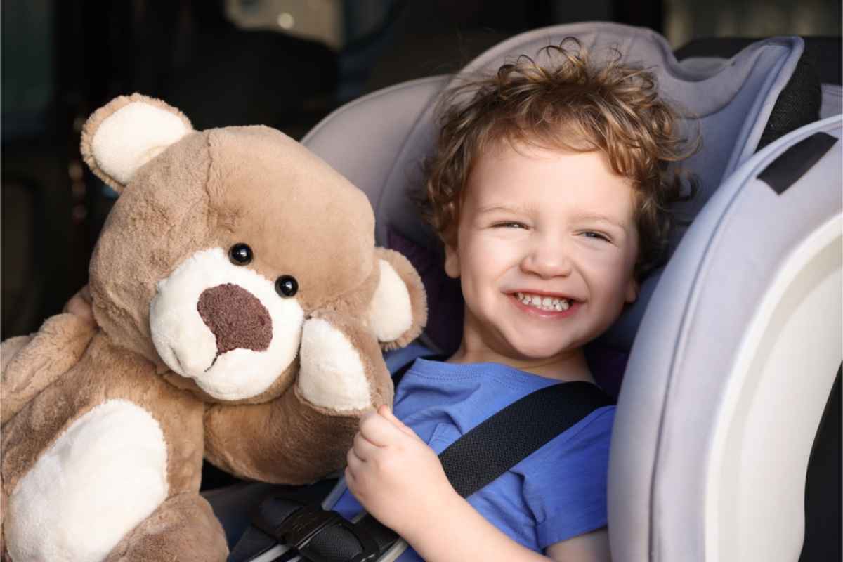 Happy kid seated in his child seat along with a teddy bear