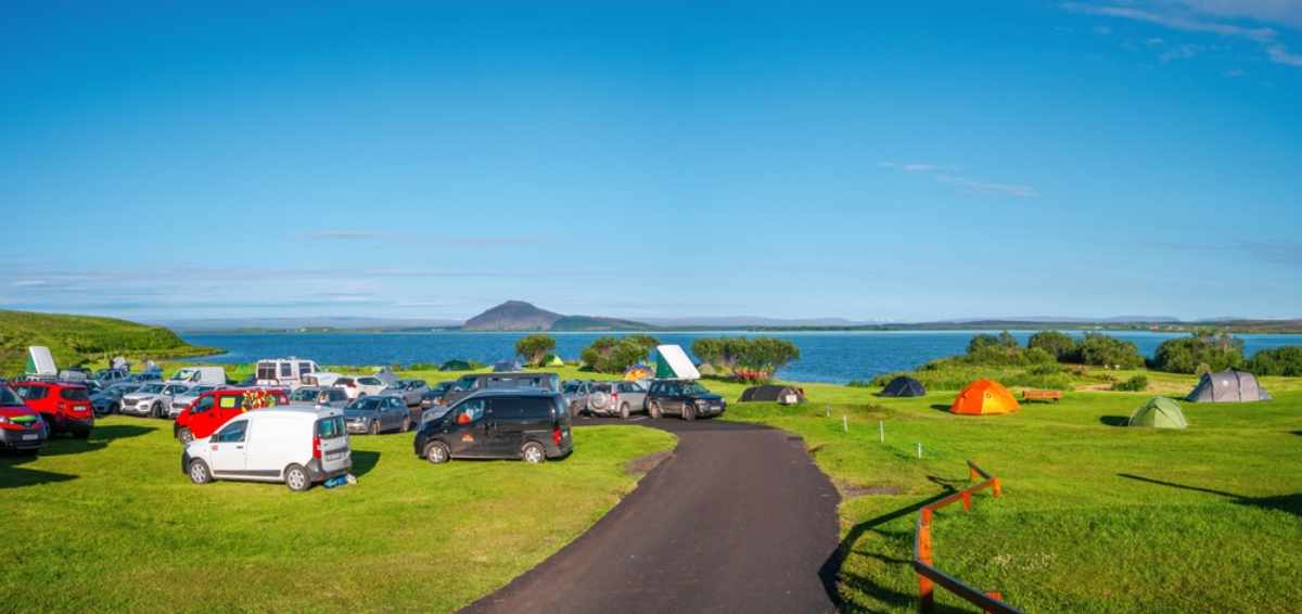 A large group of vehicles, including campervans and motorhomes, are camped in Iceland under the July sun.