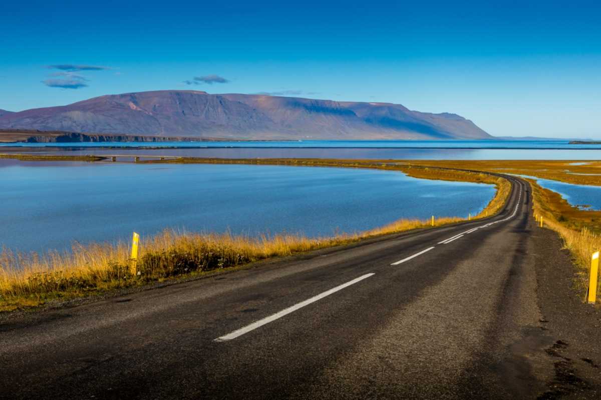 Ring Road in Iceland curving beside calm blue water with mountains in the distance