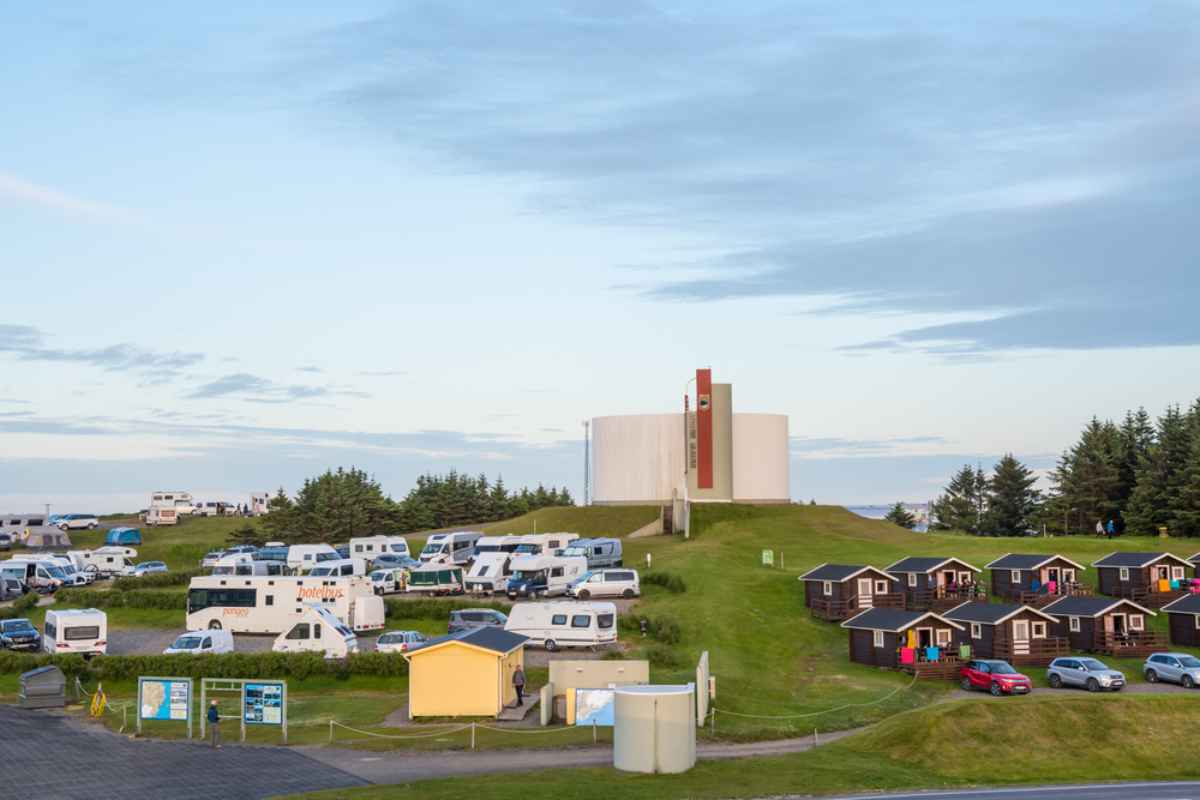 Campsite in Iceland with campervans, cabins, and a modern church on a grassy hill.