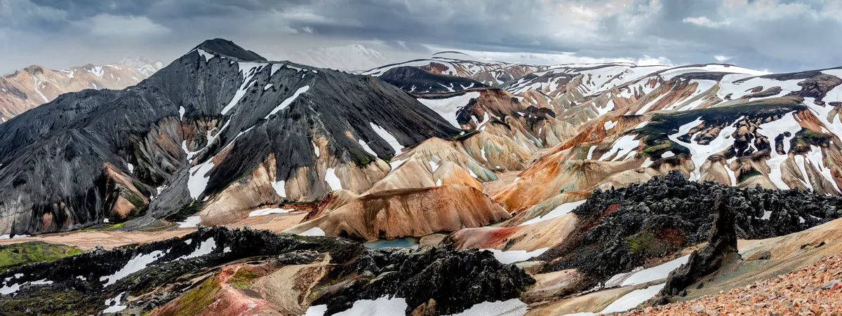 A dramatic panoramic view of the Landmannalaugar region in Iceland, showcasing the vibrant and multicolored rhyolite mountains. The landscape is chara