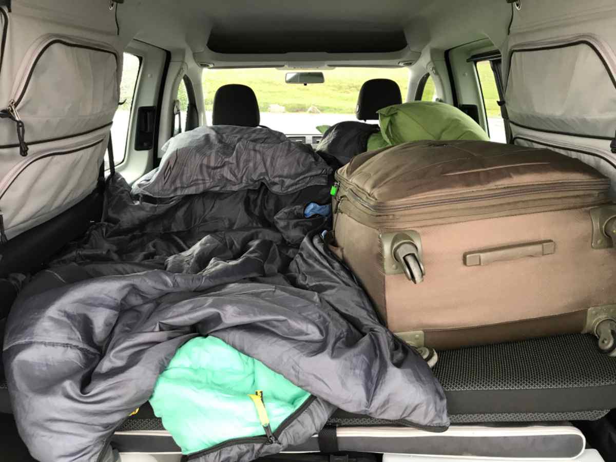 Sleeping bags and a large suitcase filling the bed platform in the back of a camper van.